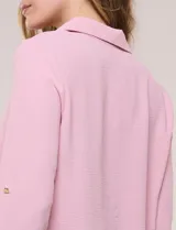 Blusa verde de calce holgado y caída fluida, confeccionada en tejido tipo crepé. Cuenta con cuello camisero con solapa, escote en V y cierre parcial al frente con tres botones metálicos. Las mangas son largas con puños abotonados.