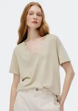 Camiseta de manga corta con cuello en V profundo, color beige claro o verde muy pálido, de corte relajado.
