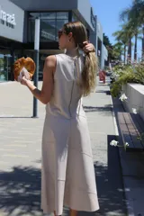 Falda midi color crudo, sin mangas, con cierre expuesto en la espalda. El diseño presenta paneles cosidos en diagonal que le dan textura y forma.