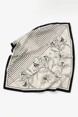 Pañuelo cuadrado con diseño dividido en dos secciones: una con estampado de líneas geométricas en ángulo y otra con ilustración botánica de flores tipo lirios en trazo negro sobre fondo crema. Presenta un borde perimetral en color negro.