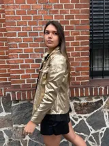 Chaqueta dorada metalizada con cuello camisero, cierre frontal con botones y bolsillos de parche en el pecho.