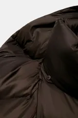 Campera puffer corta de color marrón oscuro, con diseño acolchado, cuello alto y capucha integrada. Presenta cierre frontal con botones magnéticos y mangas largas con puños elásticos.
