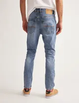 Pantalón jean celeste de corte slim fit, con arrugas en la parte superior de las piernas.