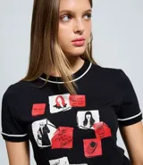 Remera negra de algodón con cuello redondo y mangas cortas con ribete blanco. Presenta un estampado frontal con motivos gráficos inspirados en la película El Diablo Viste a la Moda, incluyendo recortes tipo post-it, ilustraciones y texto.