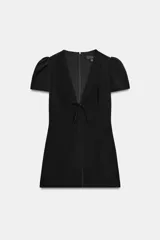 Vestido corto negro con escote en V profundo, manga corta abullonada y detalle de lazo en el delantero. Cuenta con cierre de cremallera oculta en la espalda.