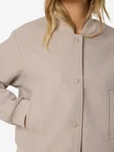 Campera bomber de corte holgado en color beige, con cuello redondo tipo baseball, cierre frontal con botones a presión, bolsillos laterales y puños y ruedo elastizados.