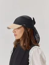 Gorro tipo pañuelo con visera rígida, confeccionado en lino. Presenta una combinación de colores negro y beige, con un diseño que se ajusta mediante nudo en la parte posterior y detalle de logo bordado en el lateral.
