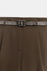 Bermuda de tiro alto color marrón, con pinzas en el delantero, perneras amplias y cierre frontal con cremallera y gancho metálico. Incluye un cinturón delgado con hebilla y estampado de efecto reptil.