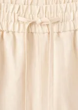 Short de lino color beige con diseño recto y detalle de franja negra en contraste en el ruedo. Cuenta con cintura elástica ajustable.