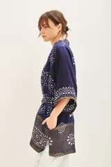 Saco tipo kimono de estilo artesanal, confeccionado en tela azul marino con estampado geométrico y floral en blanco y detalles metalizados. Presenta solapas anchas, mangas largas, lazo ajustable en la cintura y bolsillos laterales.