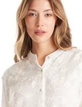 Blusa de algodón con diseño de broderie floral, cuello a la base, cierre frontal con botones y mangas largas amplias.