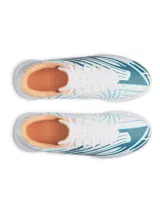 Championes de fútbol Under Armour Shadow Select 4 Turf, diseñados para césped artificial. Presentan un diseño aerodinámico en color blanco con detalles en azul petróleo y acentos en naranja. Cuentan con empeine sintético texturizado para mejor control, mediasuela Charged Cushioning para amortiguación reactiva y suela de goma con tacos multidireccionales.
