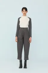 Pantalón gris de corte cropped, con pinzas, costuras a contratono y tablas en los laterales sostenidas con cuatro botones.