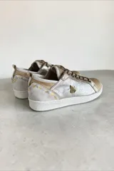 Championes de cuero de diseño artesanal, combinados en tonos plateado, dorado y natural. Presentan detalles pintados a mano por Carolina De Cunto, cordones al tono, suela de goma blanca y aplique metálico con logo en el lateral.