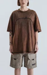 Remera de cuello redondo con calce oversize, confeccionada en algodón con proceso de teñido batik artesanal en tono óxido. Presenta costuras visibles y diseño de paneles en la parte superior.