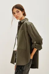 Camisa de estilo militar confeccionada en canvas de algodón, con corte oversize, cuello clásico, cierre frontal con botones y bolsillos laterales. Presenta aberturas en los costados y mangas con ajuste de botón.