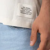 Remera oversize de lino entramado color blanco off-white, con cuello redondo, mangas cortas de hombro caído y etiqueta aplicada en el borde inferior.