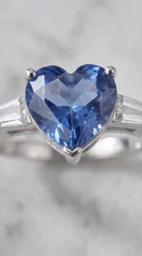 Anillo de plata 925 con piedra central en forma de corazón color azul y detalles laterales de circonias rectangulares tipo baguette.