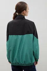 Campera de tela avión con diseño color block en negro y verde, con detalles de franjas blancas en las mangas. Presenta cierre frontal completo, cuello alto, puños y ruedo elásticos, y logo bordado en el pecho.