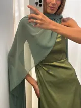 Vestido largo de fiesta color verde, confeccionado en tafeta con brillo y gasa. Presenta un diseño de un solo hombro con una capa de seda liviana integrada que permite diversas formas de uso, aportando movimiento y elegancia.