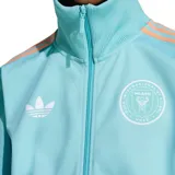 Campera deportiva Adidas color celeste con detalles en salmón. Presenta cierre frontal, cuello alto, logo de Adidas y escudo del Inter Miami CF bordados en blanco. Diseño con tres rayas en color salmón a lo largo de las mangas.