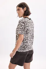 Remera de manga corta con estampa animal print en tonos beige, tostado y negro, cuello redondo negro y corte recto.