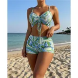 Conjunto de traje de baño de tres piezas con estampado de hojas tropicales en tonos blanco y negro. Incluye un top tipo tankini con cordón ajustable en el centro, un short de tiro alto y una camisa abierta de manga larga tipo salida de baño.