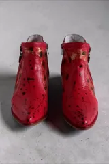 Bota corta de cuero rojo con diseño pintado a mano, inserciones laterales de cuero nonato dorado y negro, taco cuadrado de madera y doble cierre lateral con tiradores metálicos personalizados.