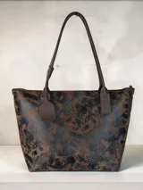 Cartera tipo tote de gran tamaño, confeccionada en cuero genuino con acabado texturizado y efecto desgastado en tonos tierra y negro. Cuenta con cierre superior metálico, interior forrado en cuero y un sujetador de asas con broche decorativo.