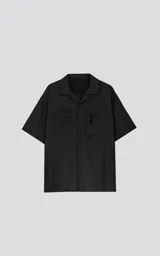 Camisa manga corta de estilo técnico, color negro, confeccionada en microfibra liviana. Presenta cuello camisero, cierre frontal con broches a presión ocultos y doble bolsillo frontal utilitario con detalles de red y cierre.