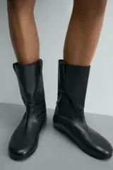 Bota de caña media fabricada en piel lisa, con diseño minimalista, tiradores laterales y suela a tono con ligero tacón.