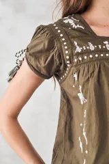 Blusa azul marino de algodón con bordados florales y de animales en blanco. Tiene escote cuadrado, mangas cortas con lazos y corte holgado.