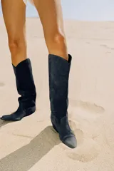 Bota alta de estilo cowboy confeccionada en serraje de color azul marino, con tacón medio en bloque y puntera perfilada. Presenta costuras decorativas en el cuerpo y diseño de calce fácil.