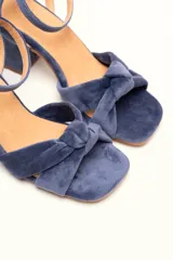 Sandalia de tacón cuadrado medio, confeccionada en terciopelo negro. Presenta un diseño de tiras cruzadas con nudo en la parte delantera y una tira ajustable con hebilla en el tobillo.