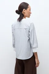 Blusa rayada en tonos beige y celeste, con cuello mao, escote en V y mangas 3/4 con puños blancos.
