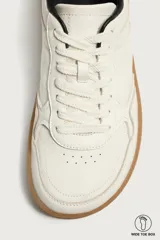 Zapatillas deportivas barefoot de hombre elaboradas en piel. Diseño en color blanco con detalles en negro y beige en el talón, y suela plana de goma marrón.