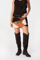 Mini falda de gamuza con diseño patchwork en tonos tierra, que combina parches de diferentes colores y texturas. Presenta una cintura con detalle de tachas metálicas doradas y un corte ajustado.