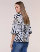 Blusa de gasa de color lila con calce holgado, cuello a la base con escote en V y cartera de botones a tono. Cuenta con fruncidos en el cuello y hombros que otorgan volumen, manga tres cuartos estilo abullonado con puño elastizado y ruedo suavemente redondeado.