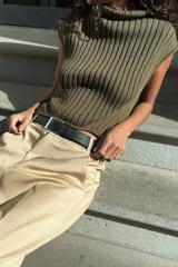 Top de tejido de punto acanalado color verde militar, con cuello alto tipo tortuga y mangas sisa. Presenta un bajo asimétrico con aberturas laterales.