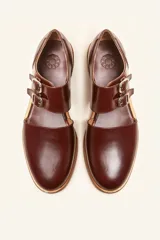 Zapato tipo oxford abierto en los laterales, confeccionado en cuero vacuno negro. Presenta doble tira con hebillas metálicas en el empeine y detalle de tachas plateadas en el contorno del talón y la puntera.