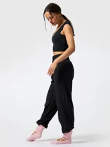Pantalón de microfibra negro, de corte estilo bombacho y silueta relajada, con cintura y puños elásticos fruncidos. Presenta costuras frontales verticales y bolsillos funcionales.