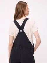 Mono de jean negro con diseño de jardinera, de corte recto y holgado, con bolsillos frontales y laterales.