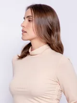 Polera color salmón de textura acanalada, cuello alto y mangas largas con ajuste fruncido en los laterales.