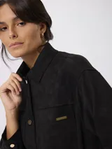 Campera de estilo camisero con efecto gamuzado, color beige, de corte recto y holgado. Presenta cuello clásico, cierre frontal con botones, mangas largas con puños abotonados y bolsillos frontales aplicados.