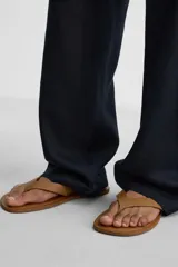 Sandalia minimalista de cuero negro, con tira delgada en el empeine y suela plana.