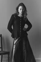 Saco de punto acanalado con cuello redondo, manga larga y cierre frontal con botones metálicos. Presenta un diseño entallado con detalle de peplum en la cintura.