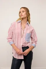 Camisa de corte oversized confeccionada en broderie de algodón con diseño combinado. Presenta un estampado de rayas verticales en tonos rojos y blancos, con detalles en contraste de color azul en el cuello, los puños y el bolsillo frontal. Posee cierre frontal con botones y mangas largas.
