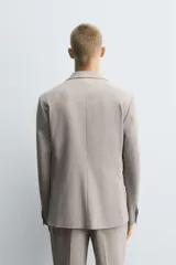 Blazer slim fit de color beige, confeccionada en tejido con lana. Presenta cuello con solapas de muesca, cierre frontal con un botón, bolsillos con solapa en la cadera y bolsillo de vivo en el pecho.