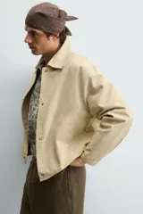Cazadora de corte relajado confeccionada en denim de algodón color beige. Presenta cuello solapa, cierre frontal con botones metálicos, bolsillos de vivo en la cadera y bajo ajustable con elástico. El interior cuenta con un forro estampado a contraste.
