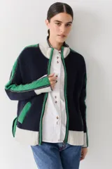 Campera de lana con cierre frontal de doble cursor y cuello alto. Presenta un diseño en bloques de color azul marino, verde y crema, con detalles de tejido trenzado en las mangas y bolsillos laterales con contraste.